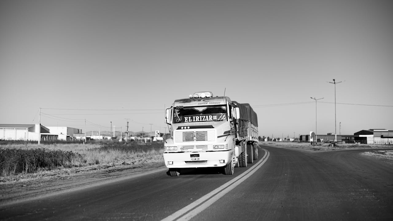 about-us Monochrome image of a truck on an empty rural road, showcasing urban life.