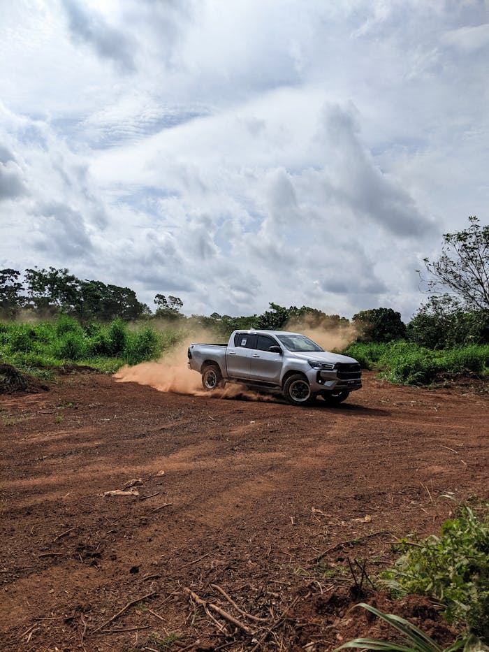 A pickup truck kicks up dust while drifting on a muddy off-road path.